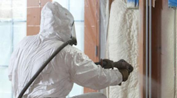 Een persoon met beschermende kleding aan die PUR-schuim aanbrengt